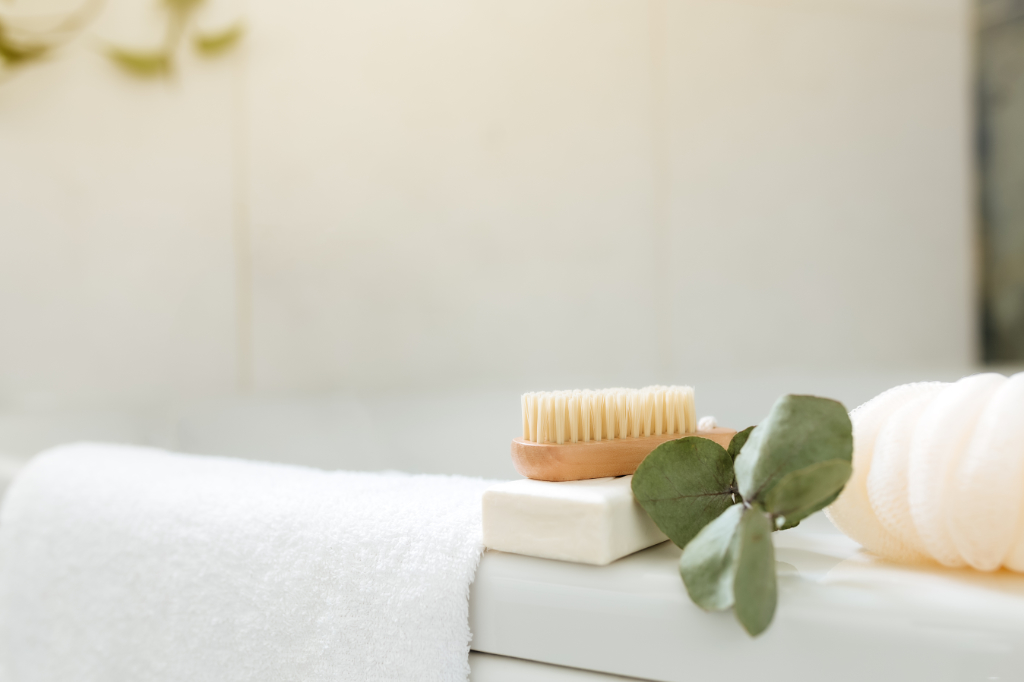 Waschbecken im weißen Badezimmer mit Badewannenzubehör. Hotelreinigungskonzept. Haushaltskonzept. Waschlappen, Seife, Fußbürste, weißes Handtuch und Eukalyptuszweig mit grünen Blättern. Stilvolles Badezimmer
