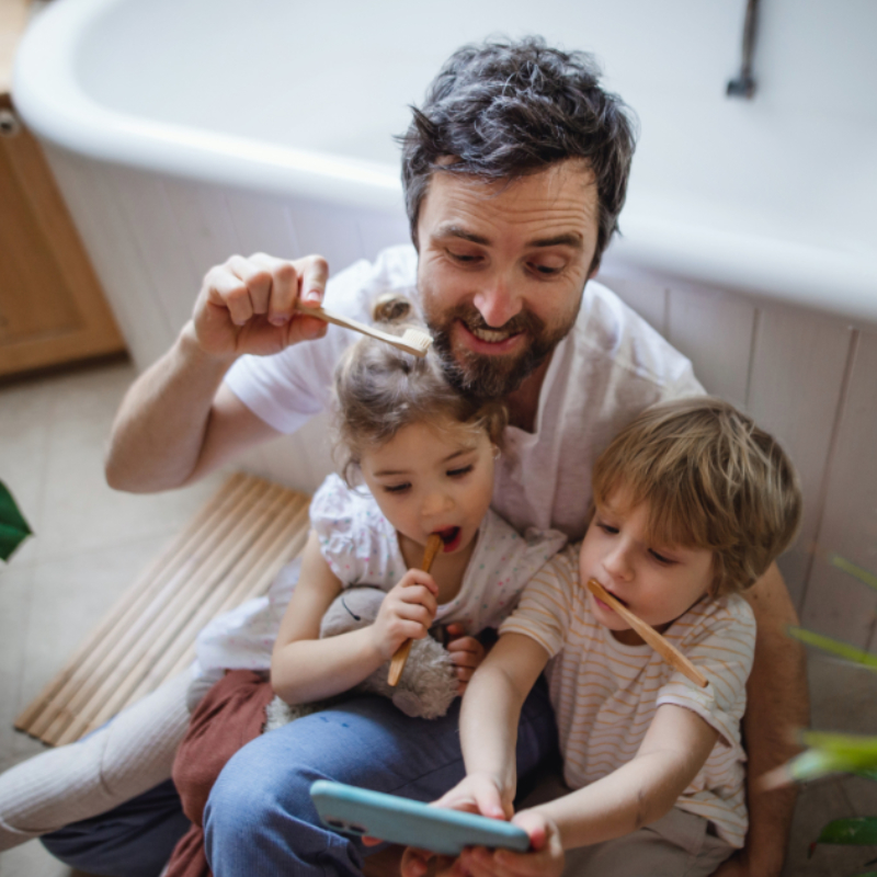 Hochwinkelansicht des Vaters mit zwei kleinen Kindern, die zu Hause drinnen Zähne putzen und Selfie machen, nachhaltiges Lifestyle-Konzept.